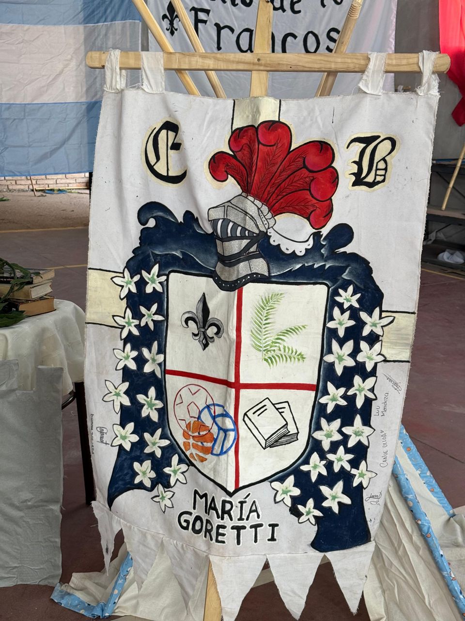 Estandarte blanco pintado a mano, con un escudo, un yelmo de penacho rojo y la inscripción María Goretti